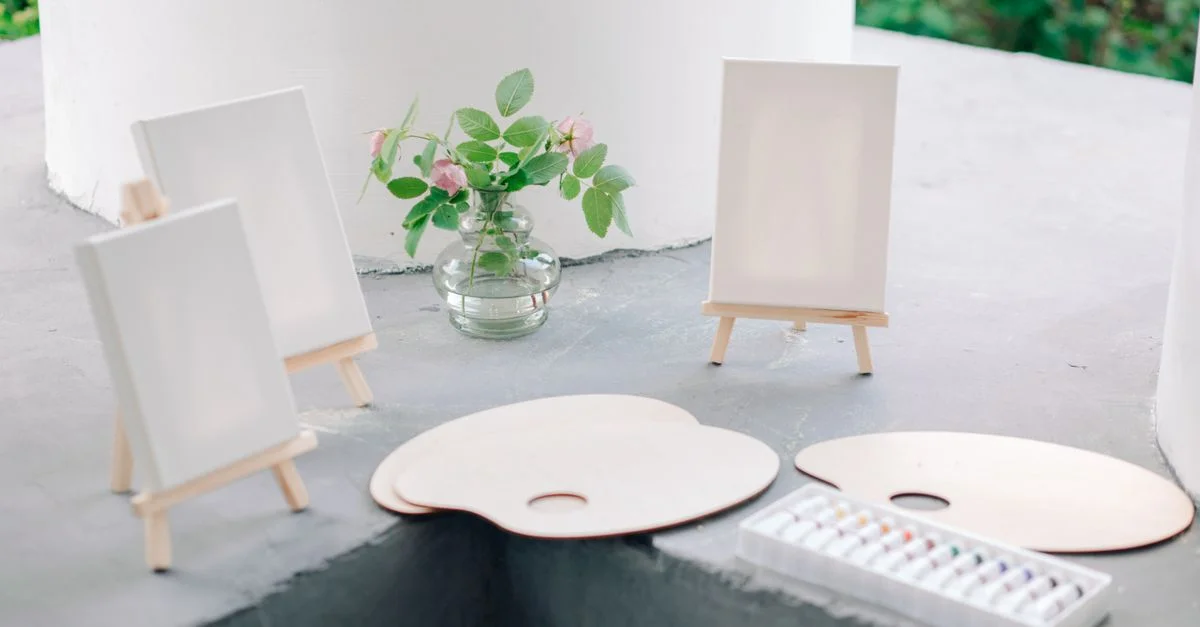 Fournitures artistiques avec des toiles vierges sur des chevalets, des palettes de peinture et un vase de fleurs.