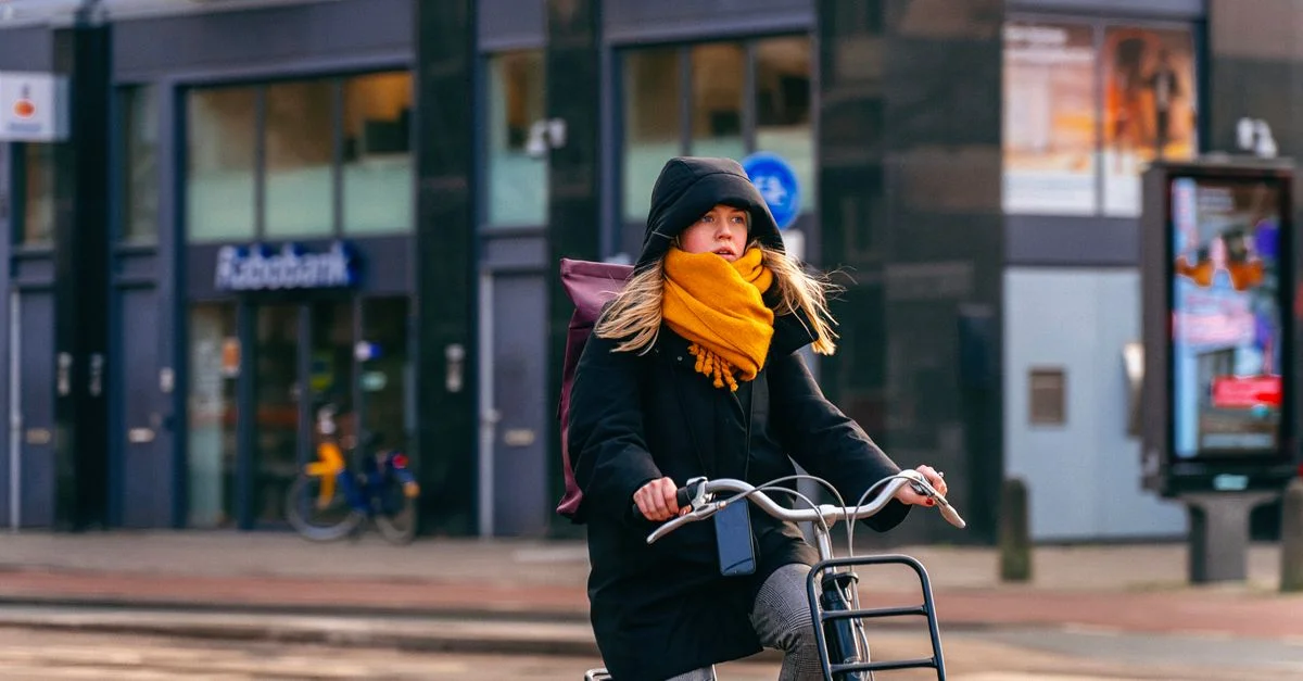 Une femme fait du vélo dans une rue d'Amsterdam, portant un hoodie et une écharpe. Scène urbaine d'hiver.